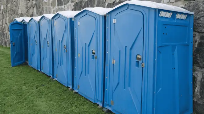 Row of blue portable toilets lined up on grass against a stone wall for event sanitation in Portland, OR