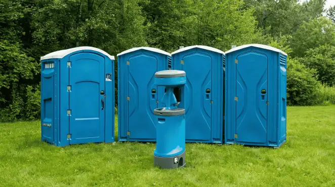 Four blue portable toilets and a matching hand washing station on grass near trees, a common sight at local outdoor events in Portland, OR