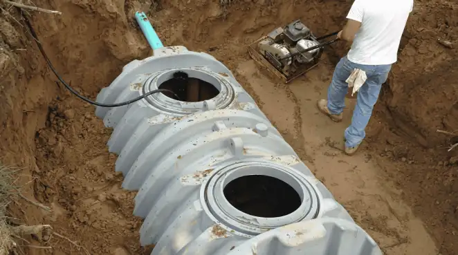 Septic tank installation showing a technician compacting soil around a new poly septic tank in an excavation pit in Portland, OR